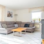 Wohnzimmer mit Ecksofa, Holztisch und Kaminofen. Durchgang zur Terrasse.