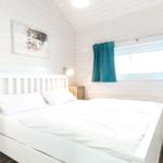 Schlafzimmer mit weißem Bett, Holzwänden und blauen Vorhängen.