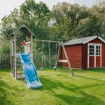 Roter Holzschuppen neben Spielplatz mit Rutsche und Schaukel.
