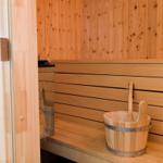 Sauna mit Holzwand, Sitzbank und Eimer mit Löffel.