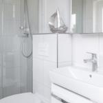 Badezimmer mit Dusche, Waschbecken und Spiegel. Silberne Segeldekoration.