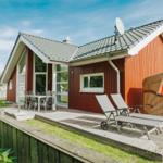 Rotes Ferienhaus mit Terrasse, Liegen und Strandkorb. Grün umgeben.