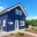 Blau gestrichenes Ferienhaus mit weißen Fenstern und Eingang. Garten mit Beeten und Holzzaun.