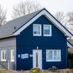 Blau gestrichenes Ferienhaus mit weißen Fensterrahmen und Vordertür. Hintergrund mit kahlen Bäumen.