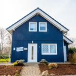 Blau gestrichenes Ferienhaus mit weißer Tür und Fenstern. Gartenweg und Beet mit Pflanzen.