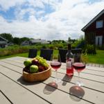 Holztisch mit Wein, Obst und Blick auf Haus und Garten.