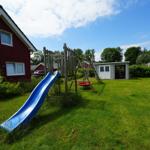 Roter Ferienhaus mit Spielplatz und blauer Rutsche im Garten.