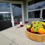 Holztablett mit Obst und Wein auf Terrasse vor Haus.