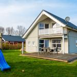 Haus mit Balkon, Terrasse und Spielplatz mit Rutsche.