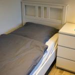 Schlafzimmer mit Bett, Nachttisch und Lampe.