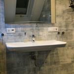 Waschbecken mit Spiegel und Duschkopf an der Wand