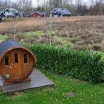 Holzbarrel-Hütte auf Holzplattform mit grünem Rasen und Hecke im Hintergrund.