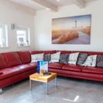 Ein Wohnzimmer mit rotem Sofa, Holztisch und Wandbild mit Leuchtturm.