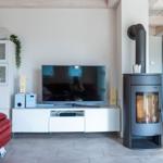 Wohnzimmer mit rotem Sofa, TV und Kaminofen.