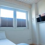 Zimmer mit Bett, Fenster und Wandfernseher.