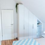 Schlafzimmer mit Dachschrägen, weißer Schrank und Bett mit Streifenbezug.