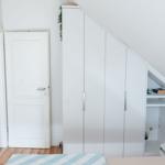 Schlafzimmer mit weißem Schrank und Bett unter Dachschräge. Tür führt in Bad.