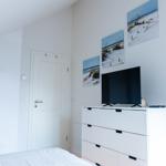 Schlafzimmer mit weißem Schrank, Fernseher und Strandbildern an der Wand.
