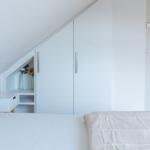 Schlafzimmer mit Dachschräge, weißem Schrank und Nachttisch mit Blumen.