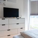 Schlafzimmer mit Bett, Schrank und Fernseher. Fenster mit Jalousie und Blick auf Balkon.