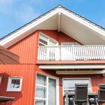 Rotes Haus mit Balkon und Terrasse unter blauem Himmel.