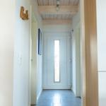 Flur mit Holzdecke, Fliesenboden und weißer Tür mit Glasstreifen.