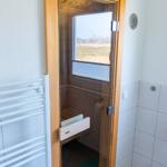Sauna mit Holzwand und Fenster, Tür mit Glas, daneben Heizung und Fliesenwand.