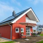 Rotes Ferienhaus mit Balkon und Terrasse mit Tisch, Stühlen und Sonnenschirm.