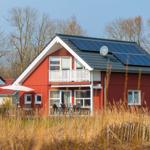 Rotes Haus mit Balkon und Solaranlage. Außenterrasse mit Tisch und Stühlen.