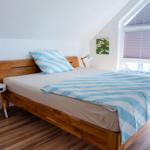 Schlafzimmer mit Holzbett, blau-weißem Bettzeug und großem Fenster mit Jalousien.