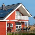 Rotes Haus mit Solaranlage und Balkon. Außenterrasse mit Tisch und Stühlen.