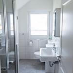 Badezimmer mit Dusche, Waschbecken und Toilette. Fenster sorgt für Tageslicht.