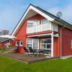 Rotes Ferienhaus mit Balkon und Terrasse mit Gartenmöbeln.