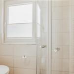 Badezimmer mit Dusche, Toilette und Fenster mit Jalousie.