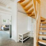 Eingangsbereich mit Holztreppe und Garderobe. Im Hintergrund Wohnzimmer mit Sofa und Fenster.