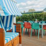 Terrasse mit Strandkorb und bunten Stühlen um Tisch