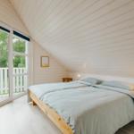 Schlafzimmer mit Doppelbett, Fenster und Balkon. Holzwände und Boden.