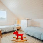 Zimmer mit zwei Betten, rotem Schaukelpferd und Fenster. Holzwände und Boden.