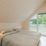 Schlafzimmer mit Dachboden, Bett, Nachttisch und Balkon mit Blick auf Bäume.