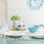 Esstisch mit blauen Schalen und Vasenblumen an weißer Wand mit Wanduhr.