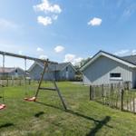 Rotes Schaukeln im Garten vor einem Ferienhaus mit Holzzaun und grünem Rasen.