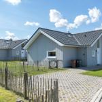 Haus mit grauem Holzschindel-Dach und weißer Fassade, umgeben von Grünfläche und Holzzaun.