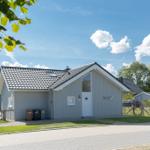 Moderne Ferienhaus mit grauer Fassade und schwarzem Dach unter blauem Himmel.