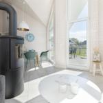 Lounge mit Holzwand, Glasfront und Kaminofen. Tisch, Stühle und TV sichtbar.