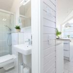 Badezimmer mit Dusche, Waschbecken und Toilette. Küche mit Küchentisch und Stühlen.