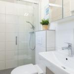 Badezimmer mit Dusche, Waschbecken und Toilette. Weiße Fliesen und Spiegelschrank.