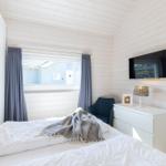 Schlafzimmer mit weißem Bett, Fenster und Wand-TV.