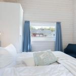 Schlafzimmer mit Bett, Fenster, Vorhängen und Sessel.