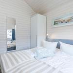 Schlafzimmer mit Bett, Kleiderschrank und Spiegel an weißer Holzwand.