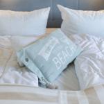 Doppelbett mit weißer Bettwäsche und einem hellblauen Kissen mit Aufschrift.